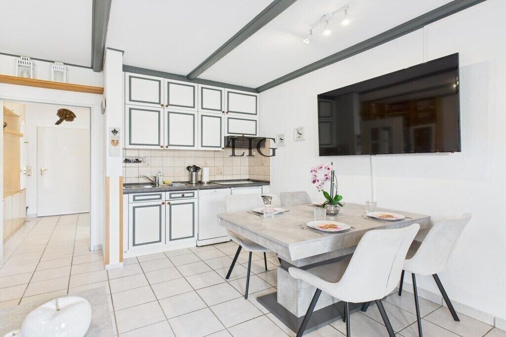 Een moderne keuken met witte kasten, een eethoek met een marmeren tafel en een groot raam.