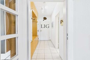 A hallway with a white door labeled 'LIG' and wooden shelving units. - Siefert holiday apartment (Langeoog)