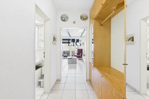 A corridor with a wooden door, white walls, and a tiled floor leading to a room with a visible sign reading 'LIG'. - Siefert holiday apartment (Langeoog)