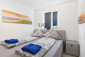 Ein Schlafzimmer mit einem Bett, Kissen, einem Nachttisch und einem Fenster.