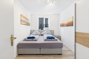 A bedroom with a bed, pillows, a window, and artwork on the walls. - Siefert holiday apartment (Langeoog)