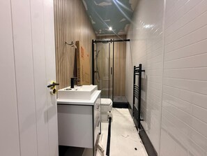 Un baño pequeño con lavamanos, inodoro y zona de ducha, todo en color blanco.