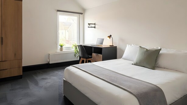 A bedroom with a bed, a desk with a laptop, a radiator, and a window. - House Sleeps 6 With Patio (Cardiff)