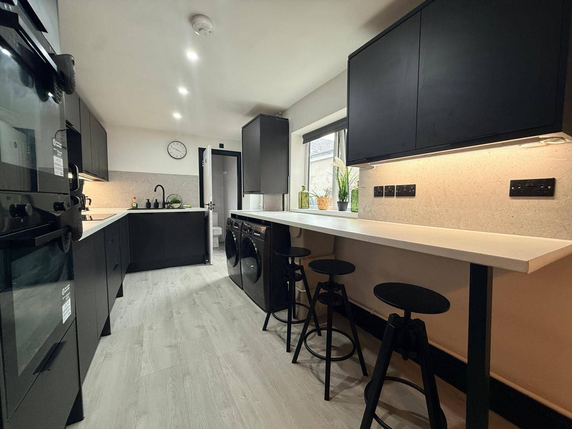 A modern kitchen with a central island, bar stools, and a large window.