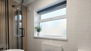 A bathroom with a freestanding bathtub, a window with a plant, and a white radiator. - House Sleeps 6 With Patio (Cardiff)