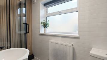 A bathroom with a freestanding bathtub, a window with a plant, and a white radiator.