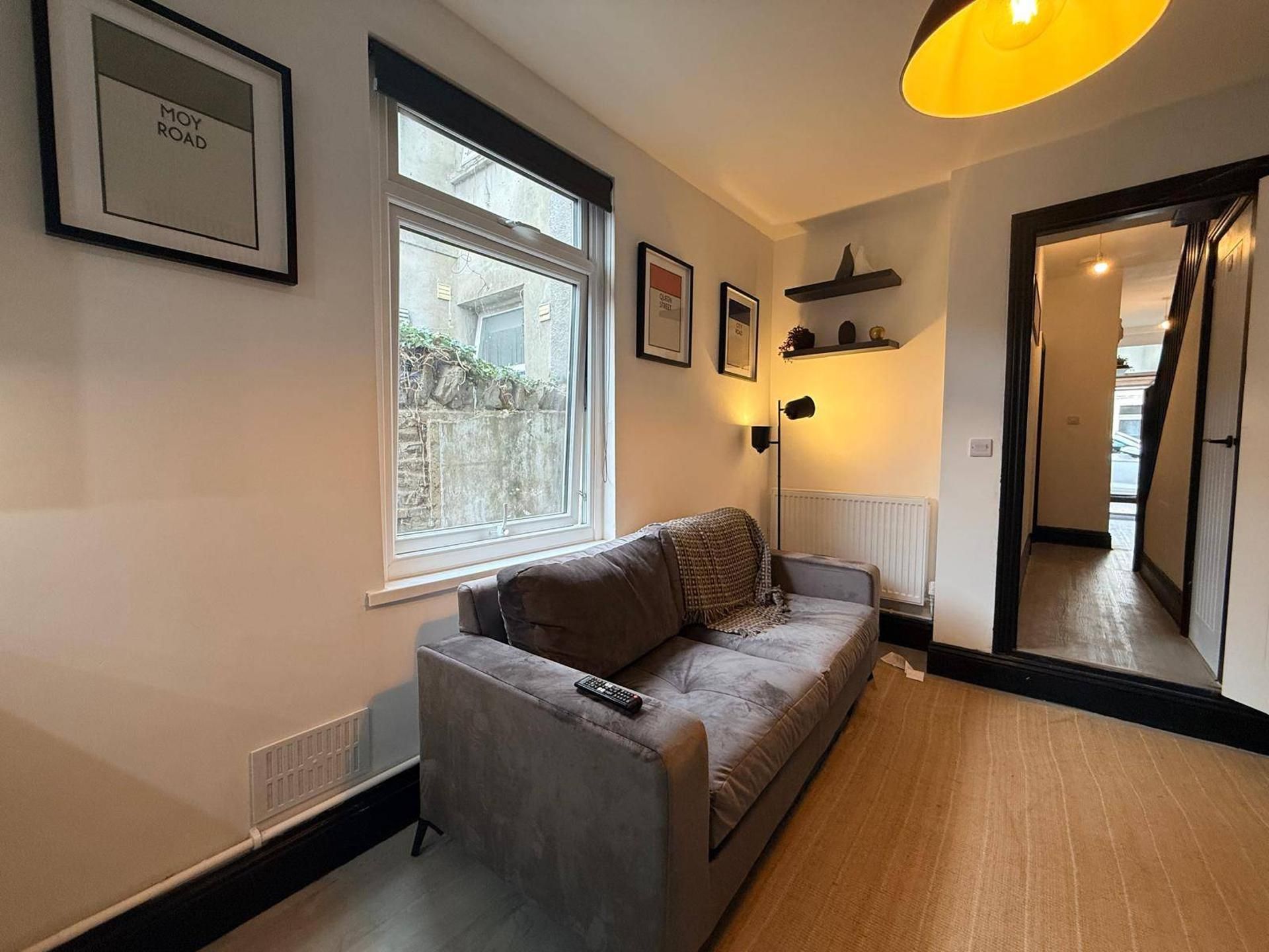 A modern living room with a grey sofa, a window, a radiator, and a hallway leading to another room.