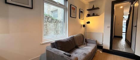 A modern living room with a grey sofa, a window, a radiator, and a hallway leading to another room.