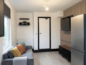 Una cocina moderna con refrigerador empotrado, una zona de comedor con banco, un sofá con cojines, un radiador y una puerta con marco negro.
