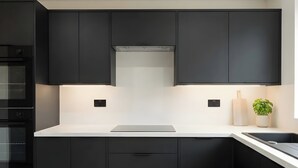 A modern kitchen with black cabinets, a white countertop, and a built-in oven. - House Sleeps 6 With Patio (Cardiff)