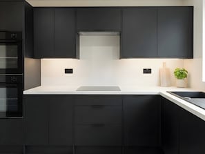 A modern kitchen with black cabinets, a white countertop, and a built-in oven. - House Sleeps 6 With Patio (Cardiff)