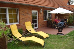 A brick house with a patio, two yellow lounge chairs, a table with a white umbrella, and a person using a laptop. - 2 on the Grafel farm (Kirchlinteln-Stemmen)