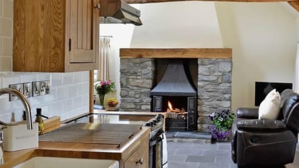 A kitchen with wooden cabinets, a stone fireplace, and a stone floor.