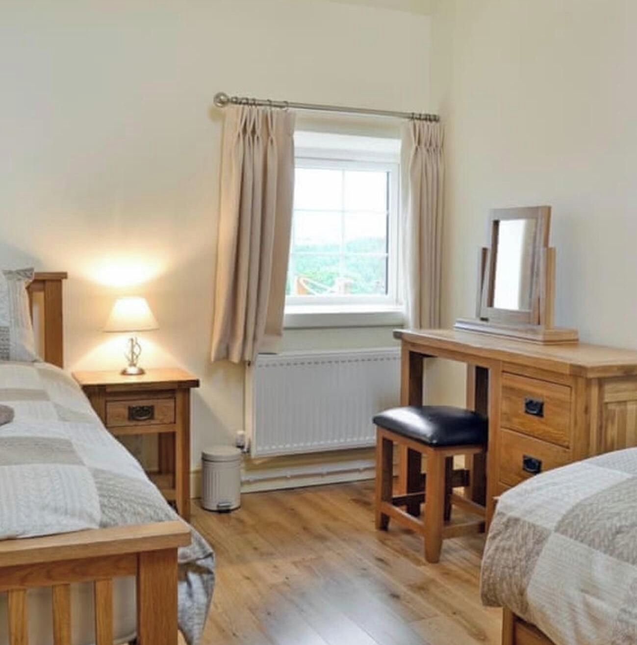 Une chambre à coucher comprenant un lit, une table de chevet, une lampe, une commode, un miroir et une fenêtre avec des rideaux.