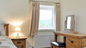 A bedroom with a bed, bedside table, lamp, dresser, mirror, and a window with curtains.