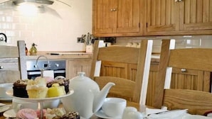 A kitchen with wooden cabinets, a white kettle, a teapot, and a table with plates of cupcakes.