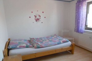 Un lit simple avec une couverture colorée, une petite table de chevet et une chaise.