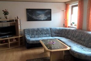 A living room with a blue sofa, a coffee table, a flat-screen TV, and a painting on the wall. - Sonja's holiday apartment (Großaitingen)