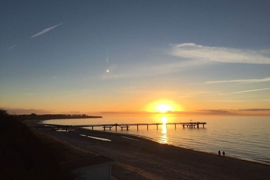 A sunset over a beach with a pier extending into the water.