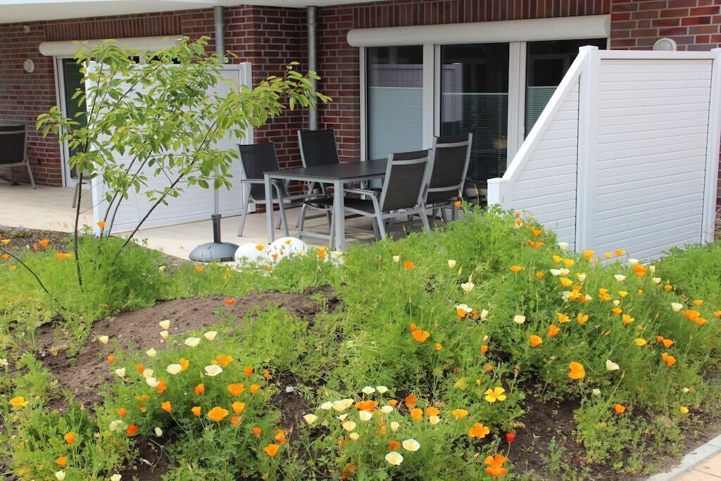 Eine Terrasse mit Tisch und Stühlen, umgeben von einem Garten mit verschiedenen Blumen.