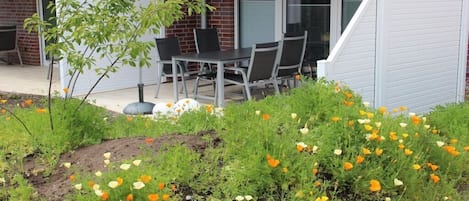 Eine Terrasse mit Tisch und Stühlen, umgeben von einem Garten mit verschiedenen Blumen.