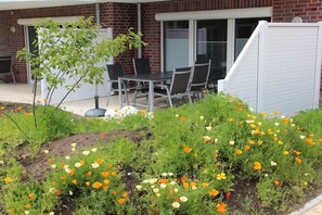 Área de pátio com mesa e cadeiras, cercada por um jardim com diversas flores.