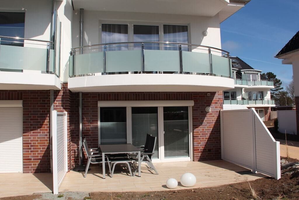 Une maison à deux étages dotée d’un balcon, d’une porte-fenêtre coulissante et d’un patio aménagé avec une table et des chaises.