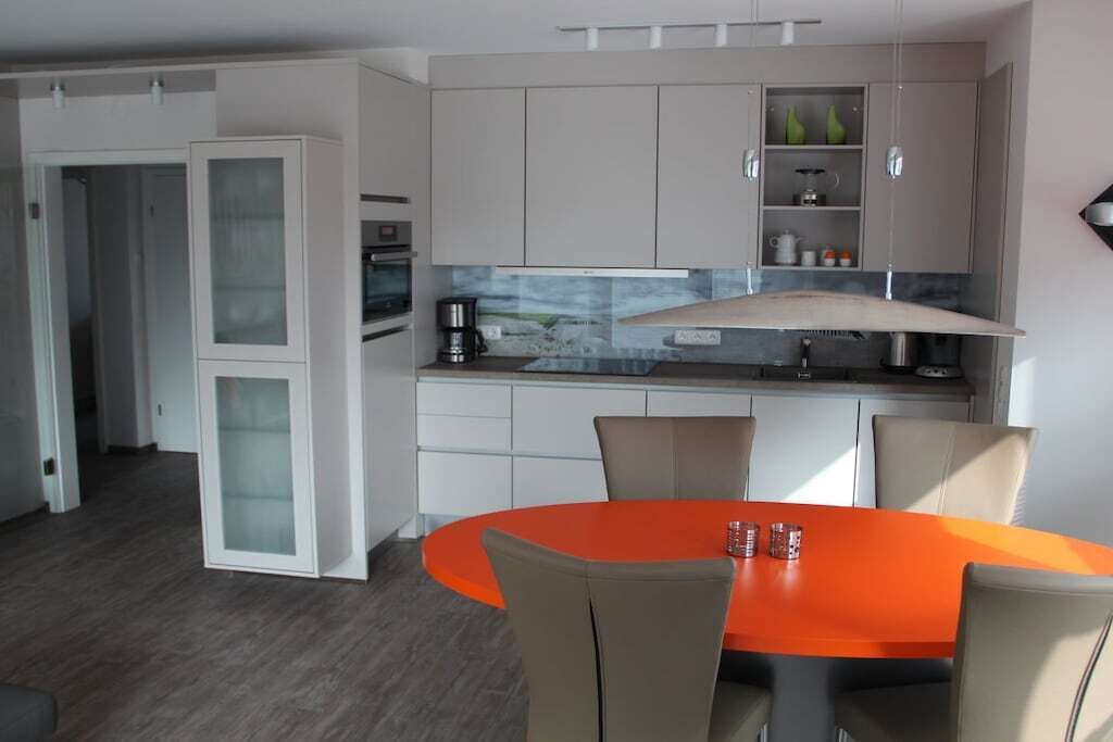 A modern kitchen with a built-in oven, a coffee machine, and a dining area with a round orange table and four chairs.