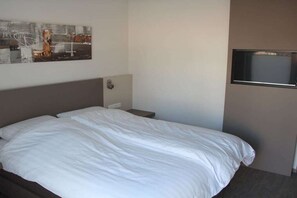 A hotel room with a bed, a nightstand, a wall-mounted TV, and a painting. - 10 in the Palais am Meer II (Cuxhaven-Duhnen)