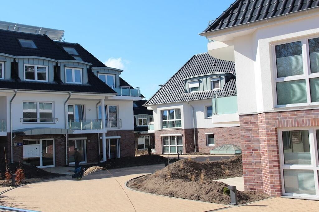 Et boligområde med moderne toetagers huse, en asfalteret indkørsel og et anlagt område med en jordhøj.