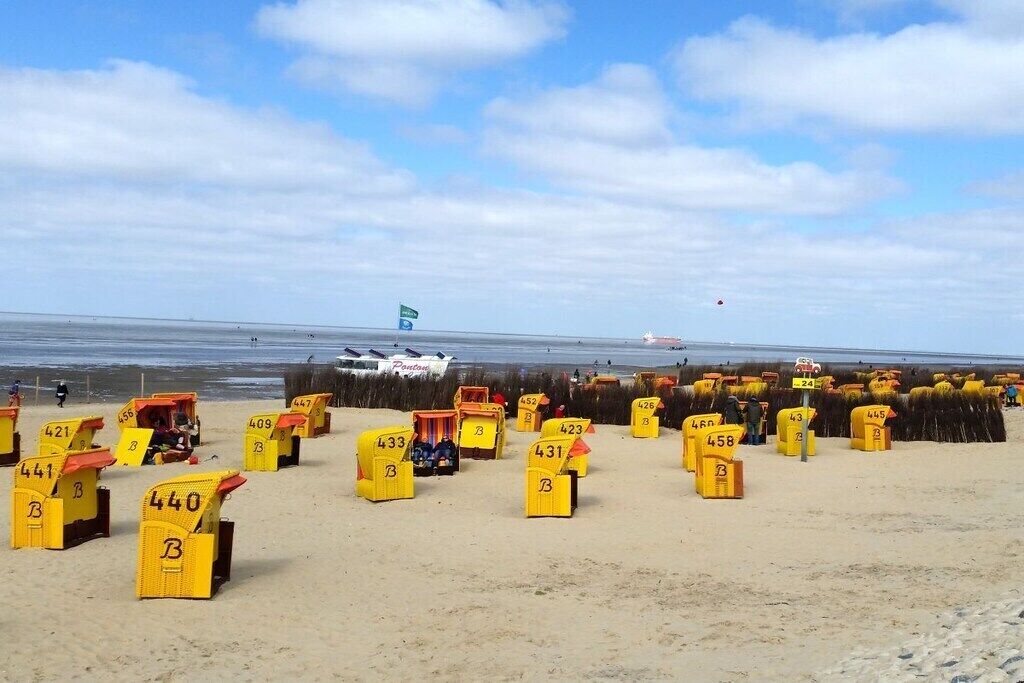 Une plage avec des cabanes de plage jaunes, chacune portant un numéro, et une vue lointaine sur la mer.