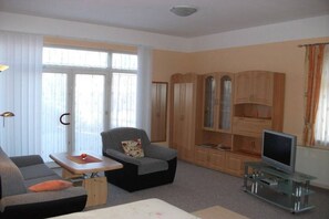 Een woonkamer met een bank, fauteuil, tv-meubel en houten kasten.