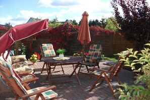 Eine Terrasse im Freien mit einem runden Tisch und vier Stühlen, umgeben von einem Holzzaun und blühenden Pflanzen.