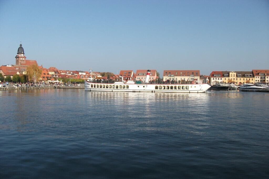 A river with a white boat, buildings with red roofs, and a tower in the background.