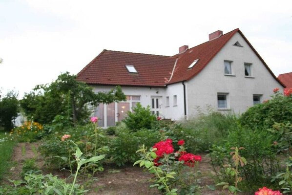 Ein zweistöckiges Haus mit einem geneigten Dach und einem Garten mit verschiedenen Pflanzen und Blumen.