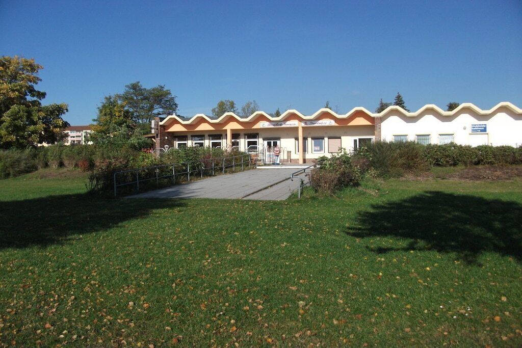 Een gebouw met een golvend dak, een verharde oprit en een gazon ervoor.