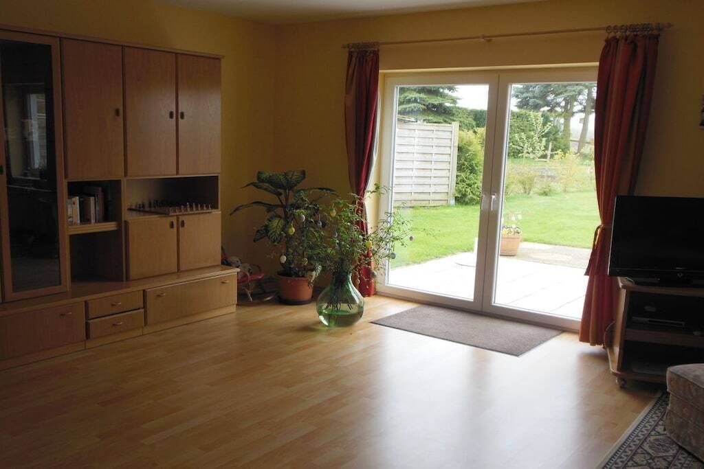 A living room with a wooden cabinet, a large plant, a television, and a sliding glass door leading to a garden.