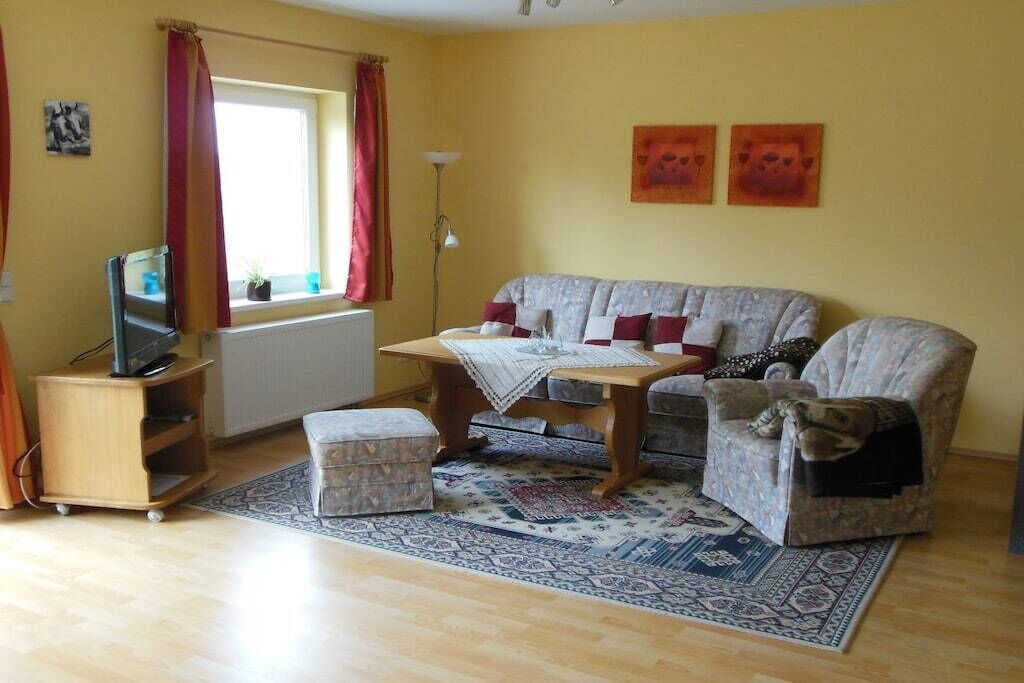 A living room with a sofa, ottoman, and a small table with a blanket.