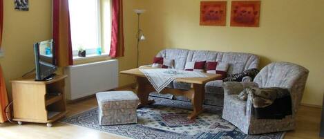 A living room with a sofa, ottoman, and a small table with a blanket.