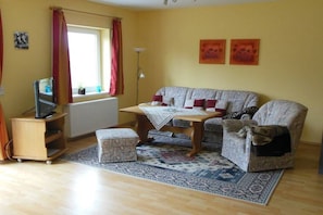 A living room with a sofa, ottoman, and a small table with a blanket. - Holiday apartment in Seedorf with barbecue (Seedorf)