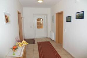 A hallway with a wooden door, a white door, and a radiator. There are pictures on the wall and a red rug on the floor. - Holiday apartment in Seedorf with barbecue (Seedorf)