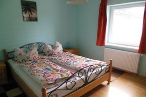 A bedroom with a bed, a nightstand, a lamp, a window with curtains, and a wall painting. - Holiday apartment in Seedorf with barbecue (Seedorf)