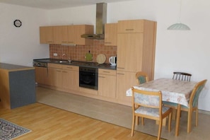 A compact kitchen with wooden cabinets, a stove, and a dining area with a table and chairs. - Holiday apartment in Seedorf with barbecue (Seedorf)