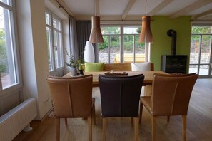 A dining area with a wooden table and chairs, large windows, and a fireplace. - Bergmannstrost 5-star holiday apartment (Sankt Andreasberg)