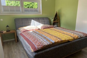 A bedroom with a bed, a nightstand, a lamp, and a window with blinds. - Holiday apartment with 1 bedroom (Fehmarn)