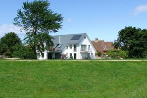 A two-story house with a sloped roof, solar panels, and a large lawn in front. - Holiday apartment with 1 bedroom (Fehmarn)
