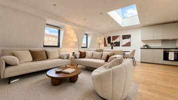 A modern living room with a sofa set, a coffee table, and a kitchen area with cabinets and a countertop.