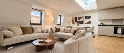 A modern living room with a sofa set, a coffee table, and a kitchen area with cabinets and a countertop.