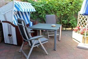 An outdoor patio with a table and chairs, a striped umbrella, and a wooden fence with greenery. - HOUSE LUV 2 - on the ground floor (Wittdün)