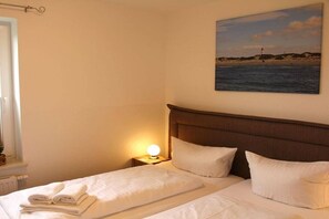 Habitació d'hotel amb un llit, una tauleta de nit amb una làmpada, i un quadre de platja a la paret.